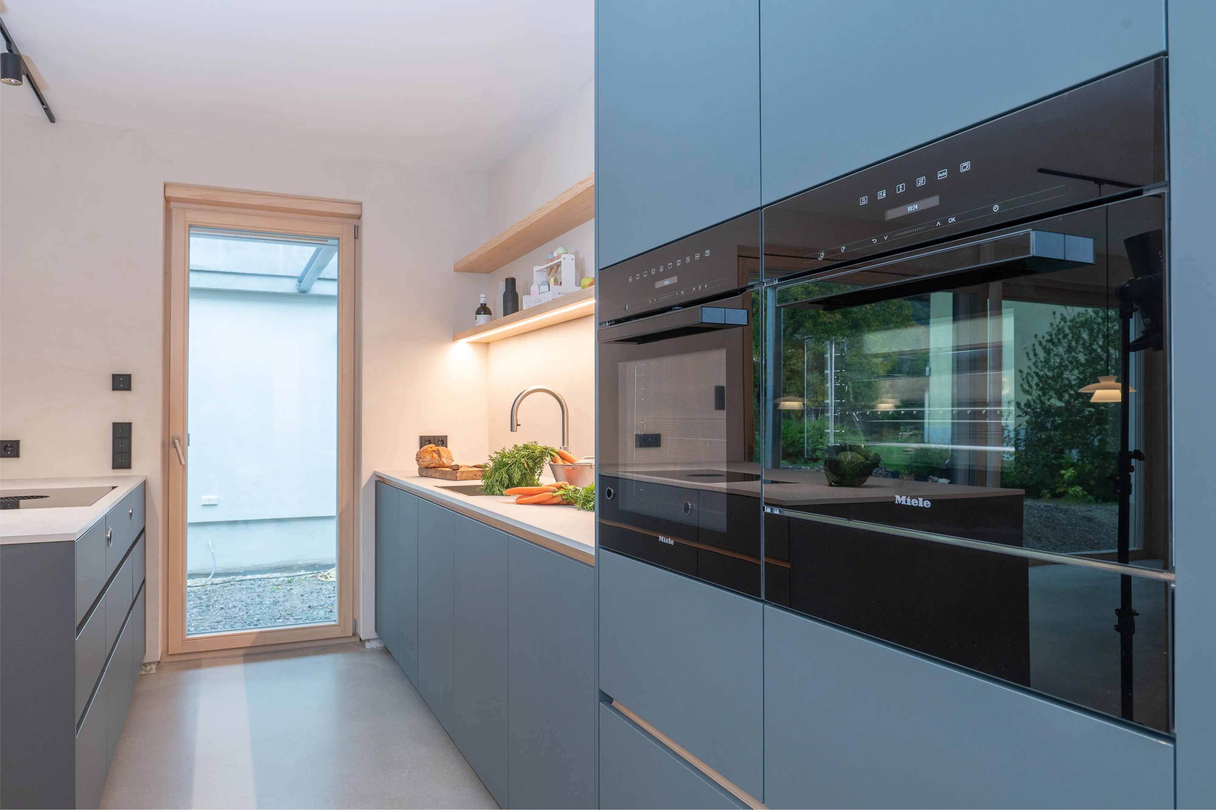 Blaue Küchenschränke mit zwei eingebauten Miele-Backöfen und heller Arbeitsplatte