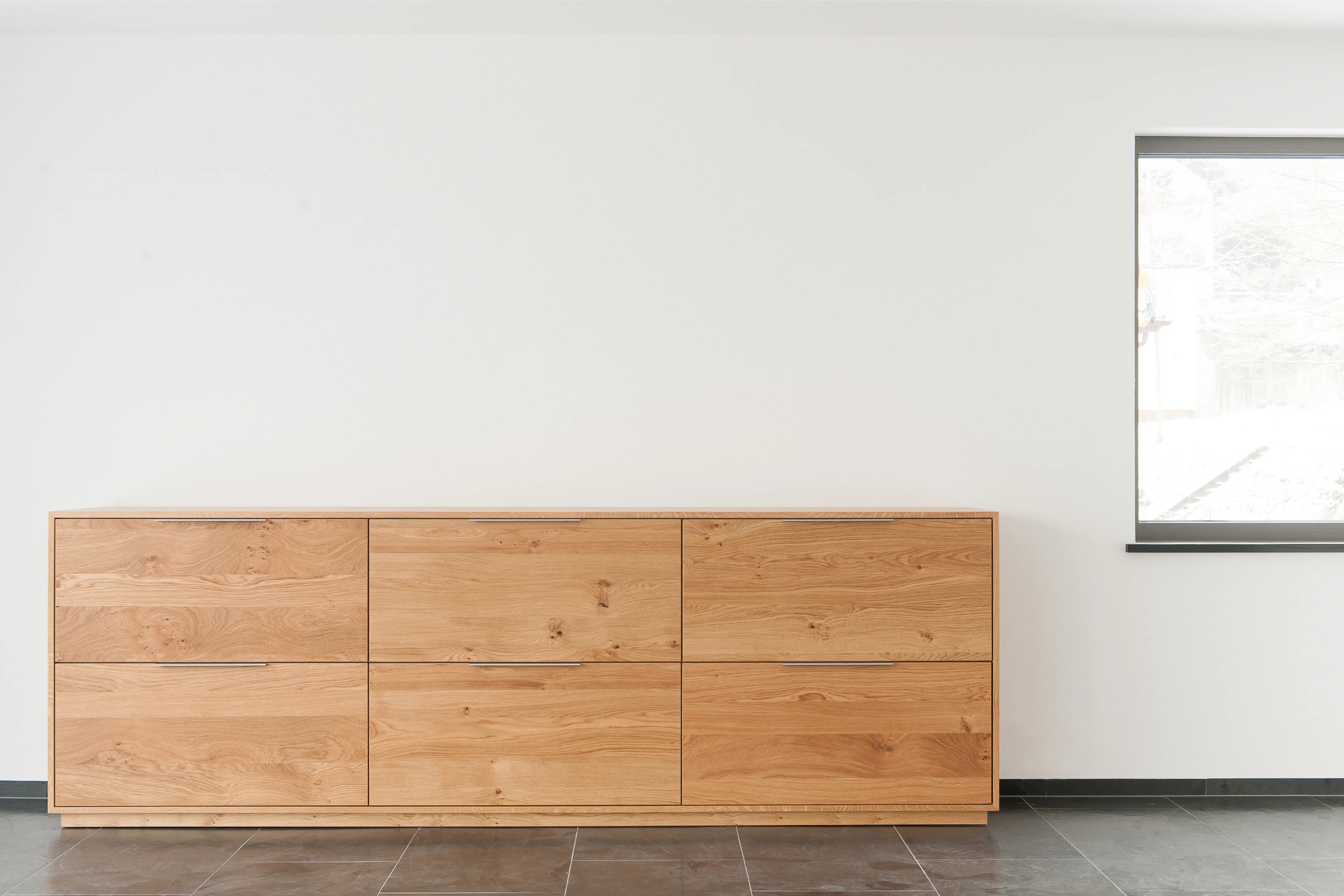 Ausführliches Sideboard aus Massivholz mit sechs großen Schubladen vor einer weißen Wand und dunklem Fliesenboden