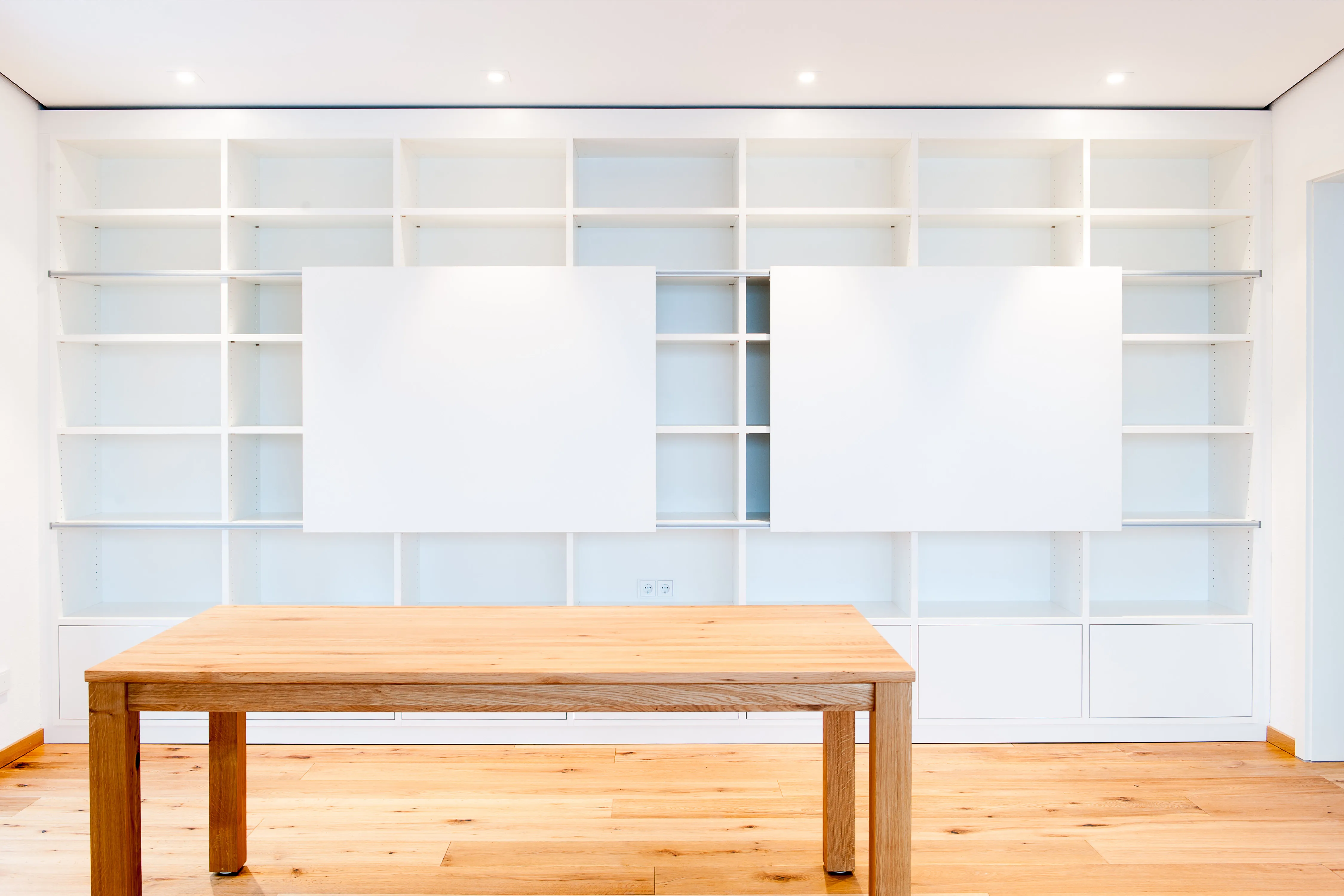 Großes weißes Bibliotheksregal mit schiebbaren Paneelen hinter einem massiven Holztisch und Parkettboden