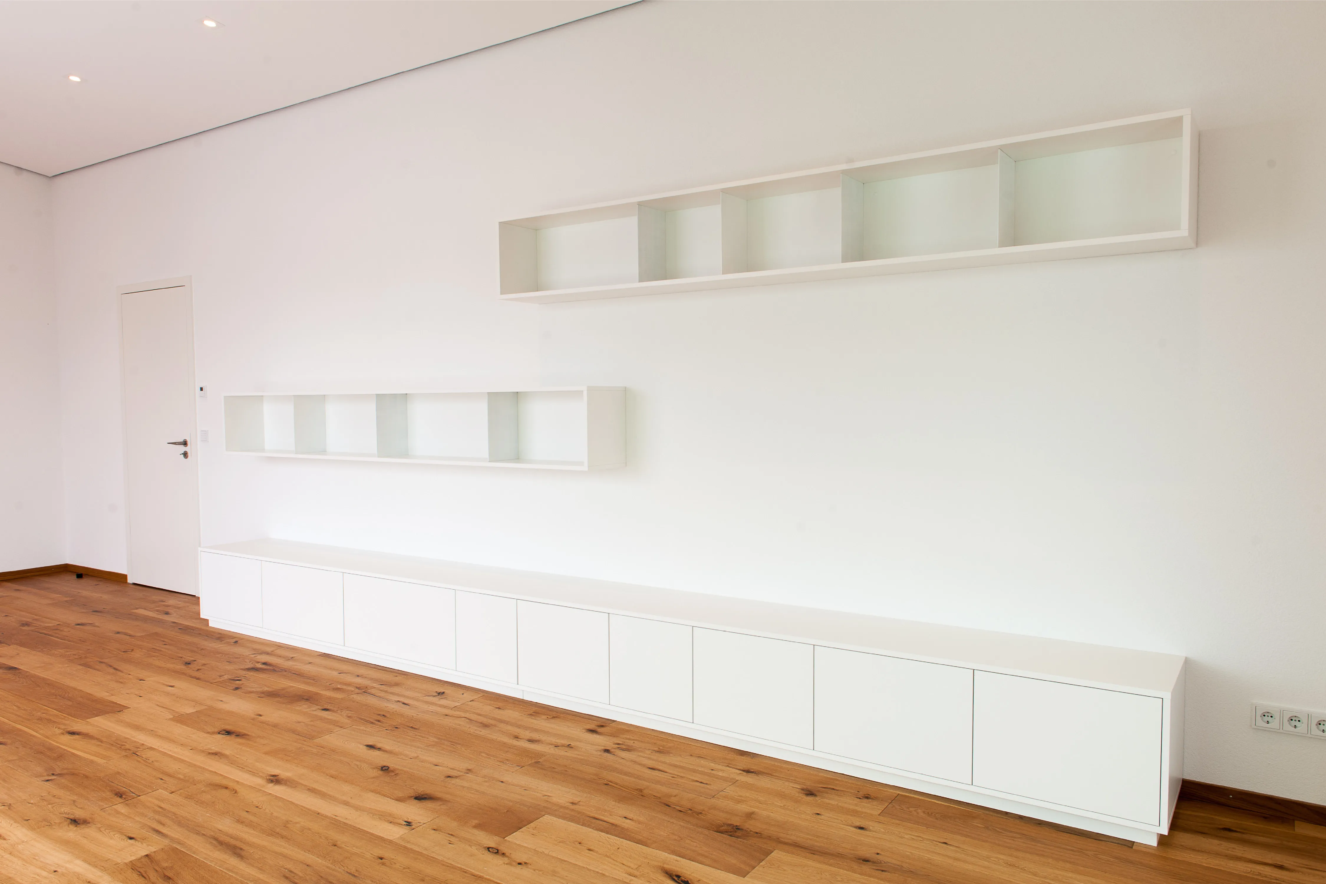 Helles Wohnzimmer mit langanhaltendem weißem Lowboard, zwei passenden Hängeregalen und Holzparkett