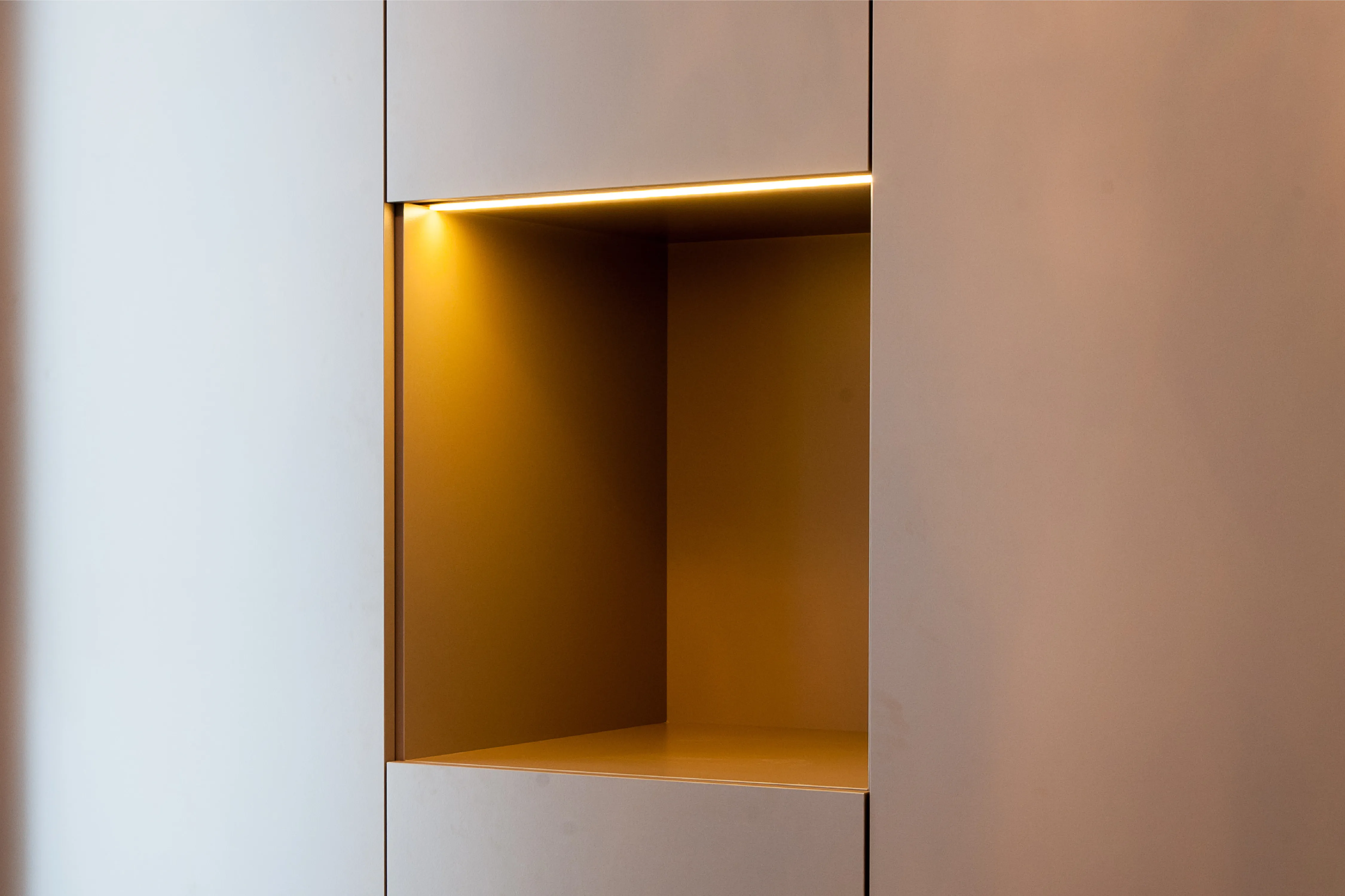 Detailansicht einer beleuchteten, warmen Nische in einem minimalistischen weißen Einbauschrank
