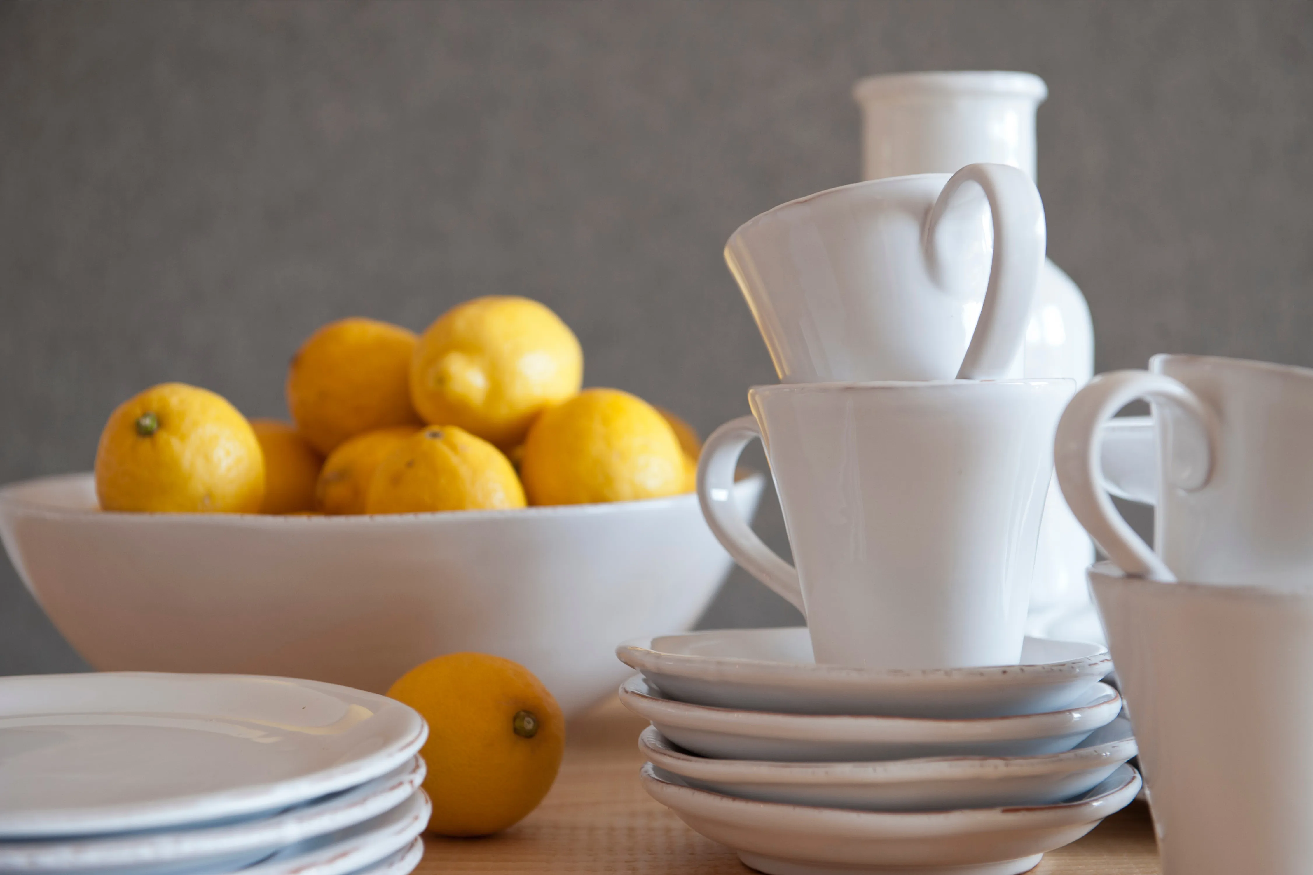 Dekoratives Arrangement von weißen Kaffeetassen, Untertellern und einer Schale mit frischen Zitronen auf einer Holzoberfläche
