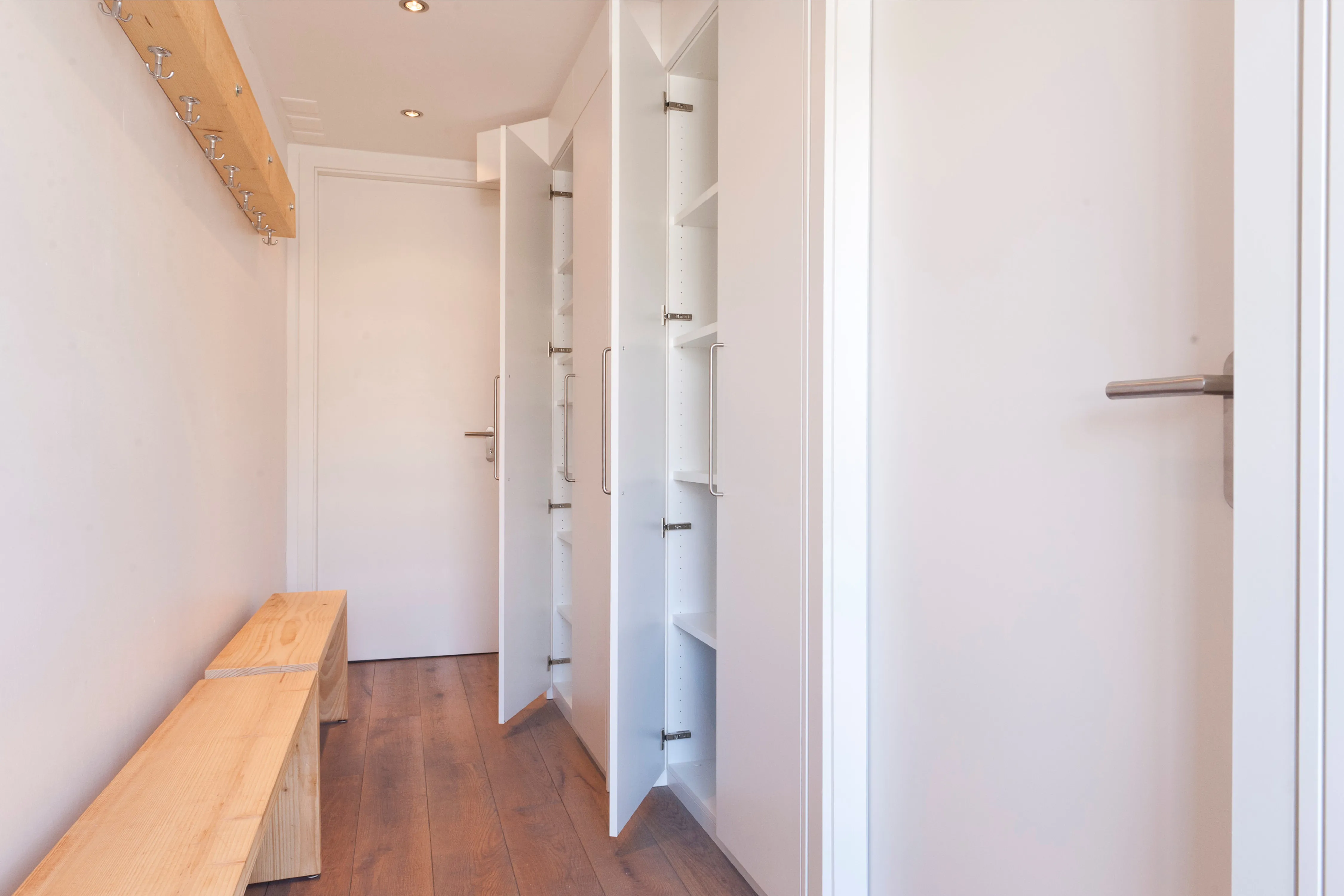 Heller Flur mit weißem Einbauschrank mit geöffneten Türen, Holzbank und Wandgarderobe