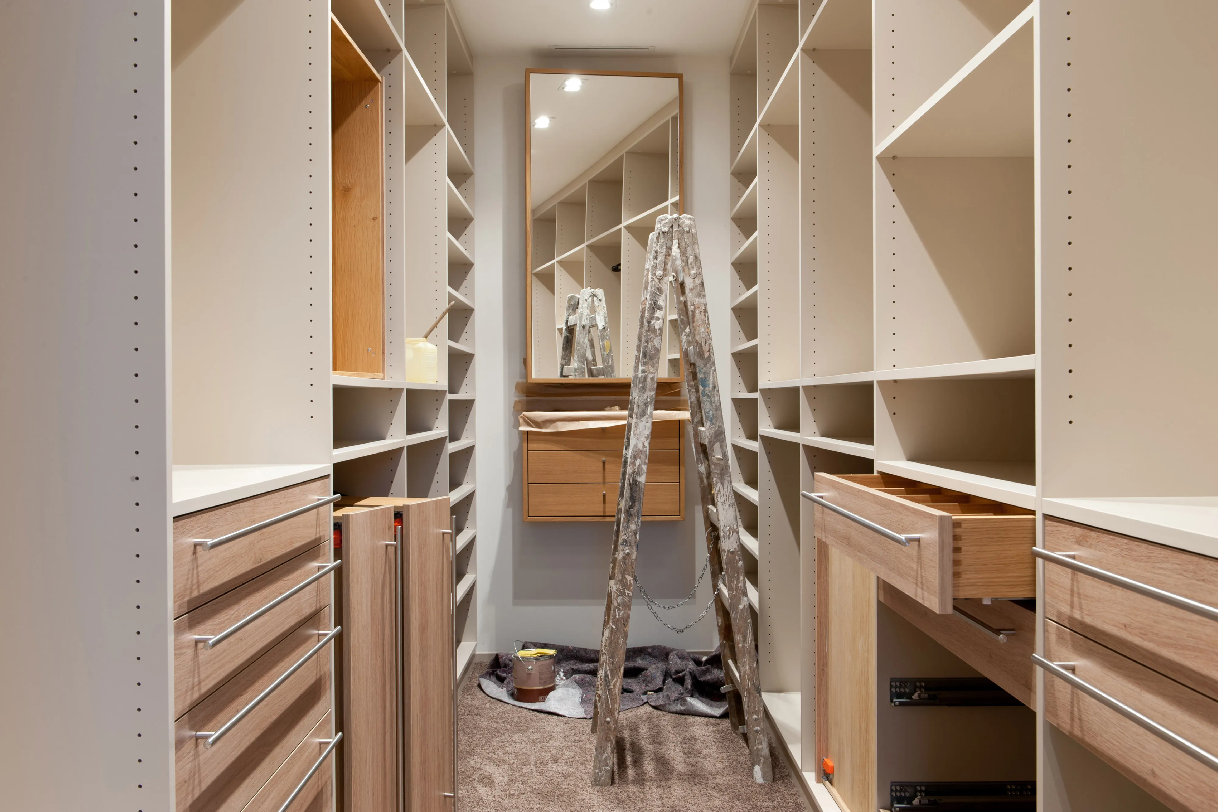 Begehbarer Kleiderschrank in der Entstehung mit maßgefertigten hellen Regalsystemen, Schubladen aus Holz und Holzleiter im Raum