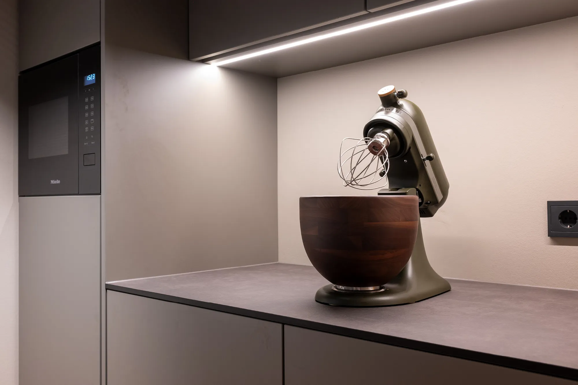 Küchen-Arbeitsplatte in Schieferoptik mit olivegrüner Küchenmaschine und Holz-Rührschüssel.
