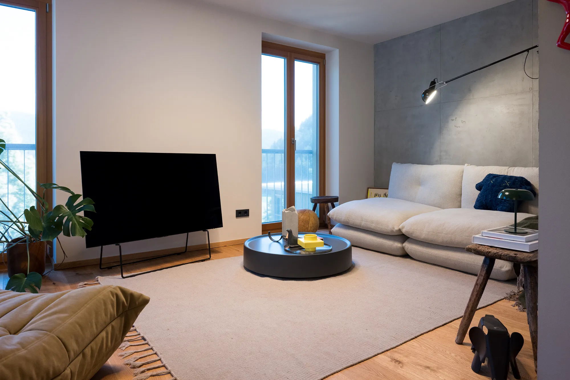 Gemütlicher Wohnbereich mit hellem Sofa, flachem Couchtisch, TV und Wand in Betonoptik.