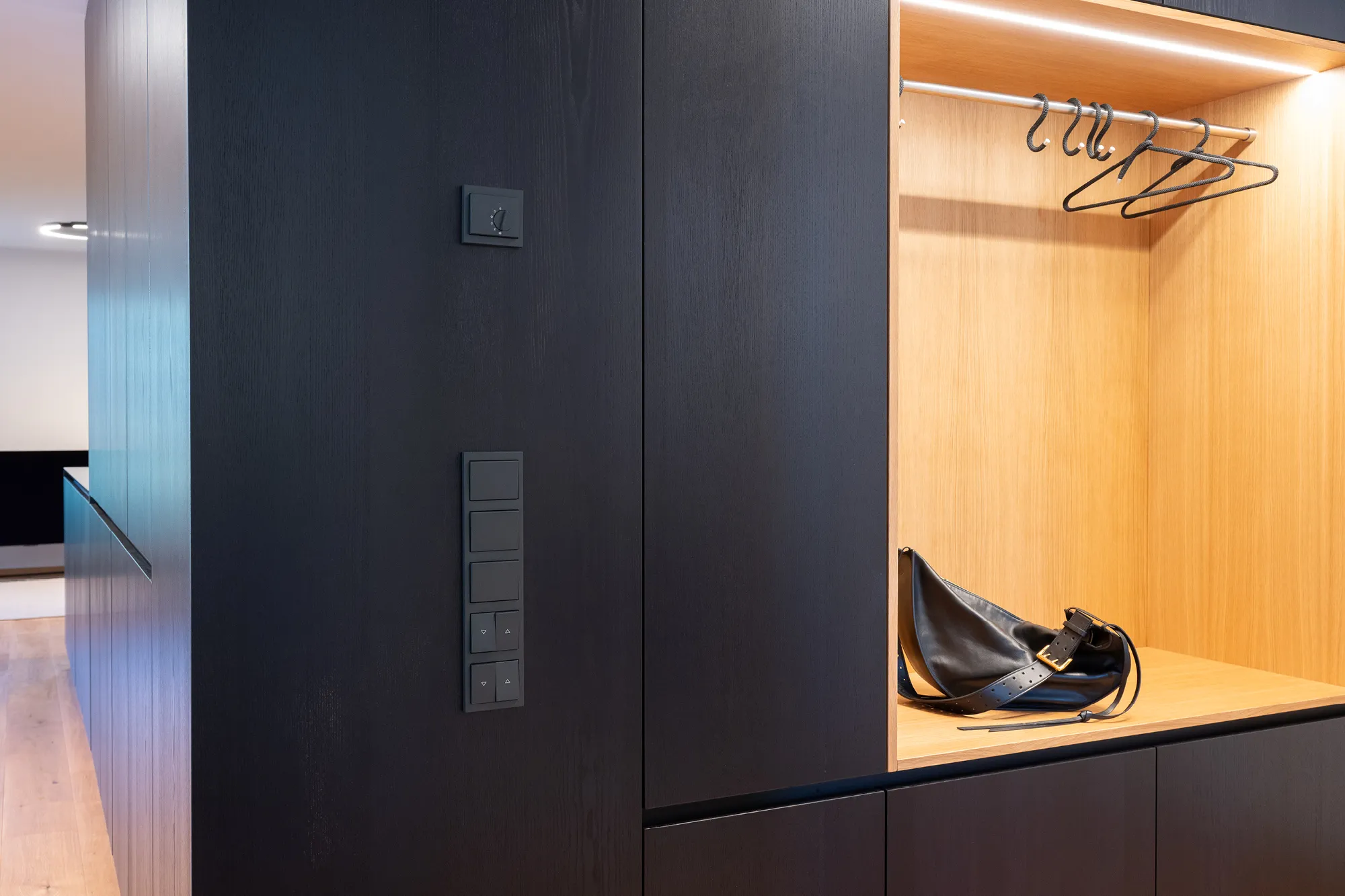Schwarzer Einbauschrank mit integrierter Garderobennische aus hellem Holz und warmem Licht.
