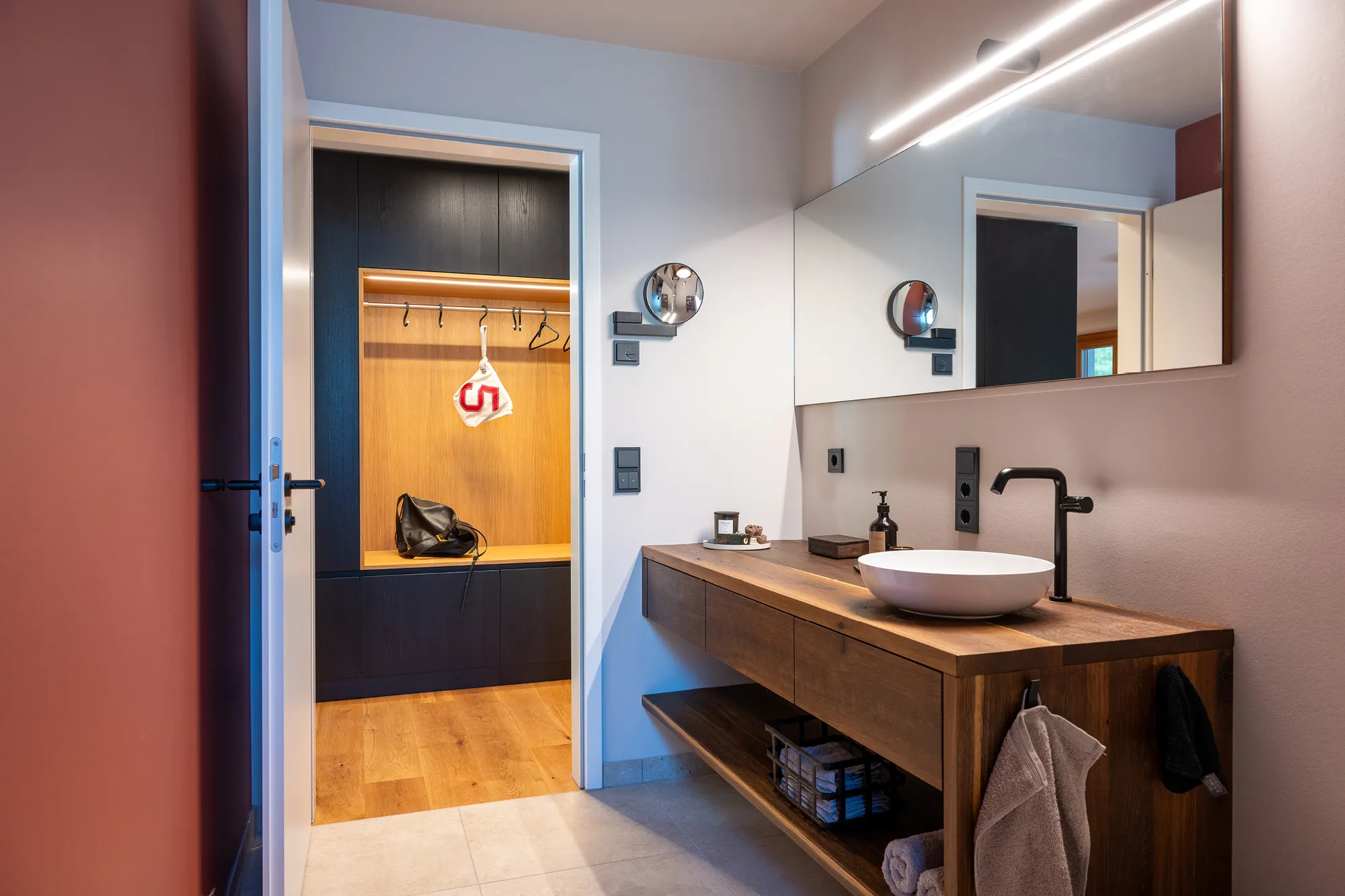Badezimmer mit Massivholz-Waschplatz, Aufsatzwaschbecken und Blick auf die Garderobe im Flur.