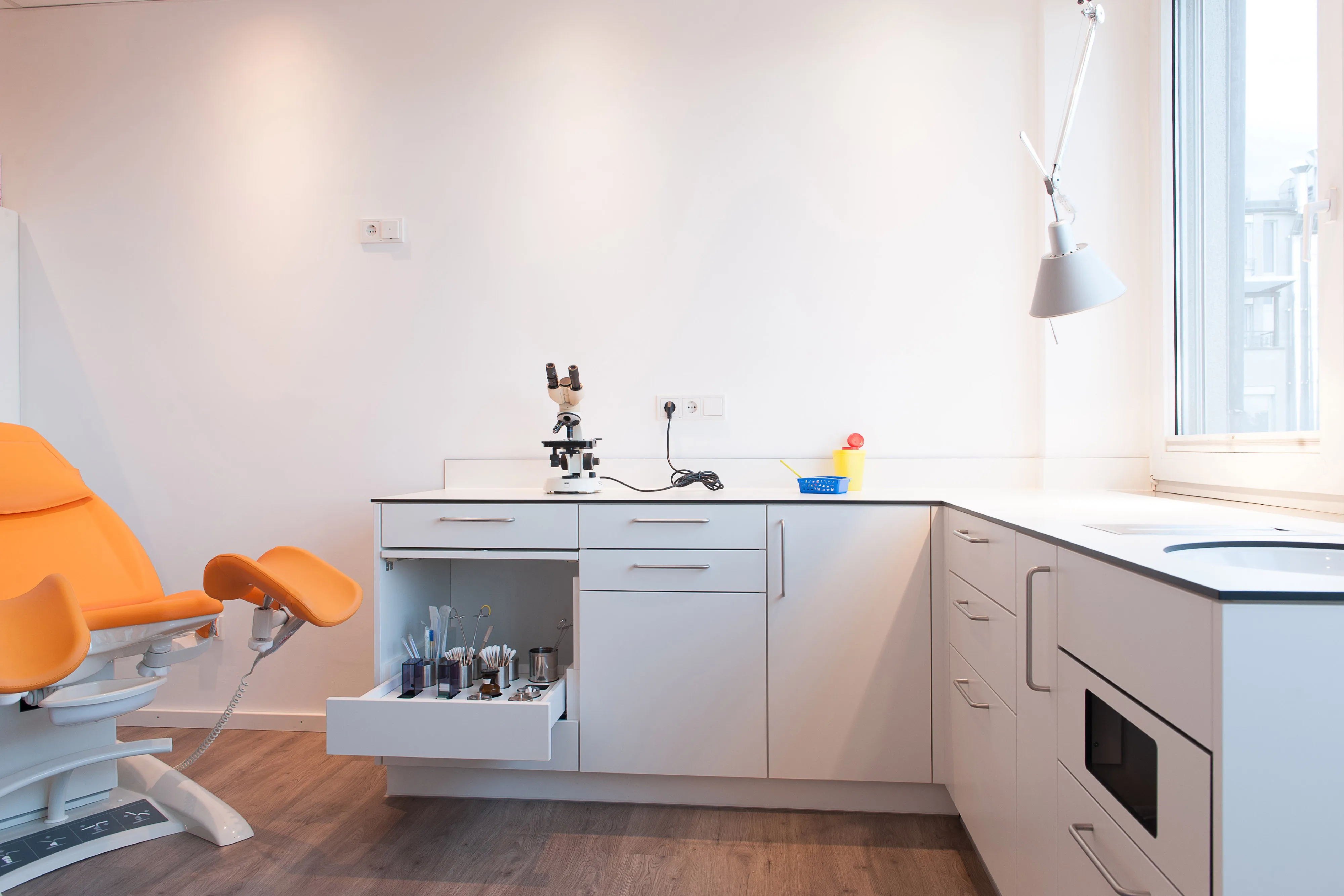 Großzügige Zeile aus weiße Praxismöbeln im Behandlungszimmer mit ausgetüfteltem Besteckauszug und Mikroskop.