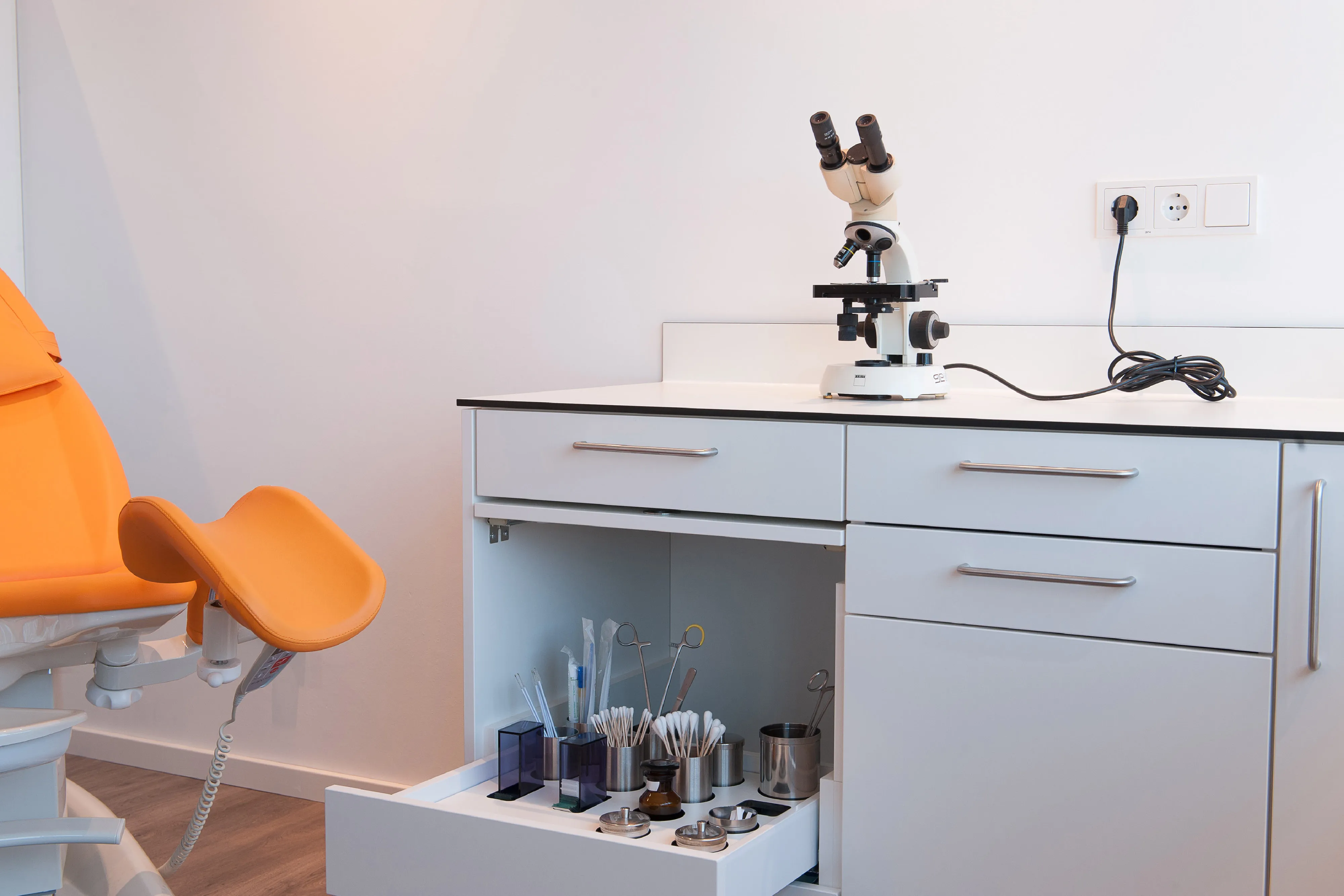 Detailaufnahme des ausgezogenen Schubfachs mit Halterungen für medizinische Instrumente und Wattestäbchen neben dem Untersuchungsstuhl.