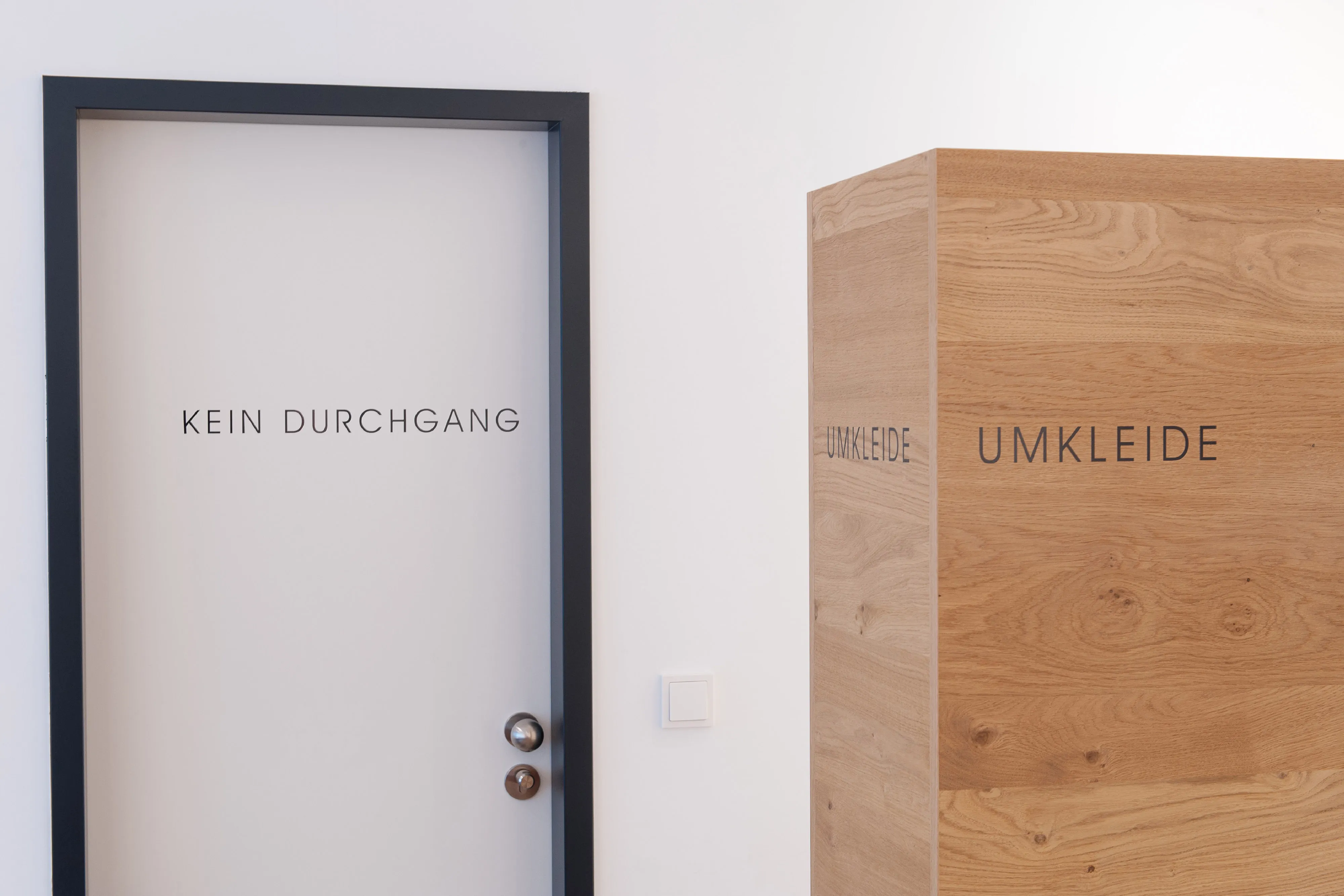 Tür mit Beschriftung „Kein Durchgang“ neben einer freistehenden Umkleidekabine aus echtem Eichenholz.