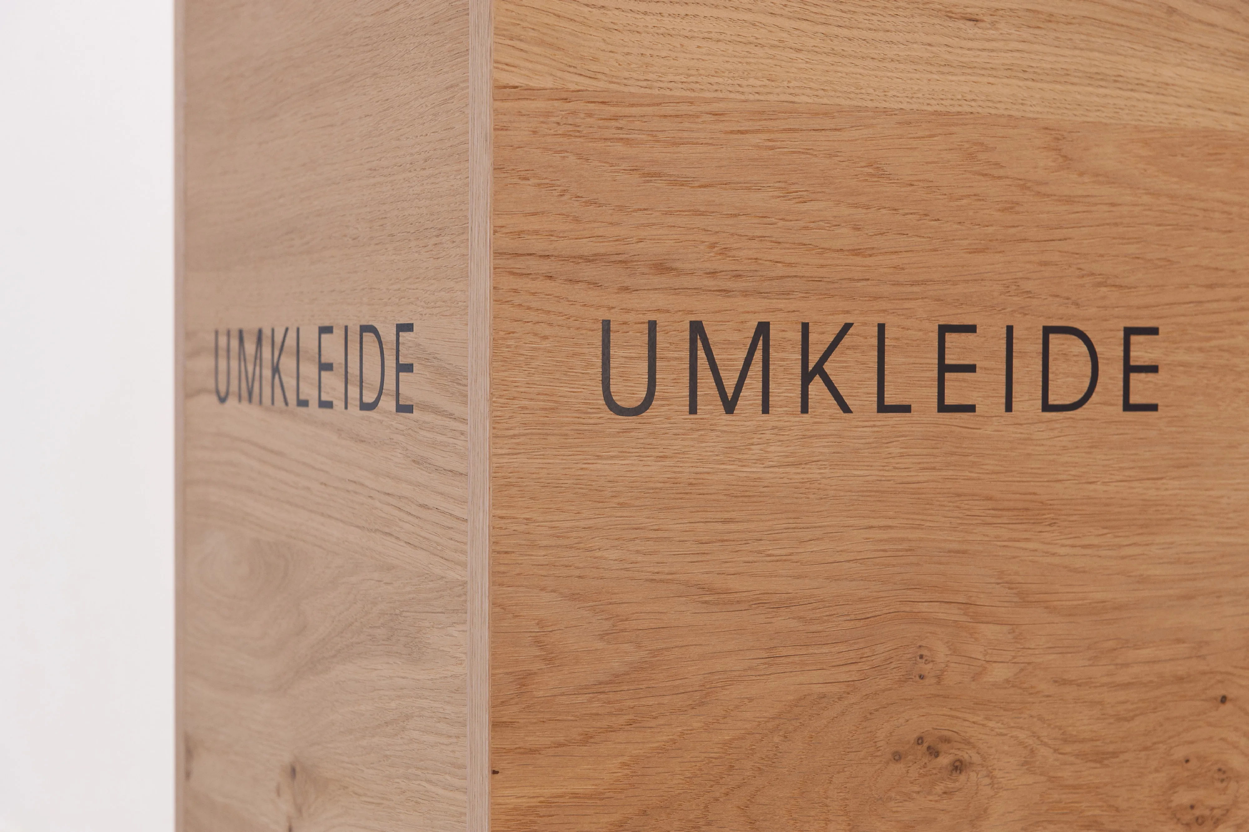 Nahaufnahme des hölzernen Umkleide-Elementes mit präziser Eckverarbeitung und sauber aufgebrachter Aufschrift „UMKLEIDE“.