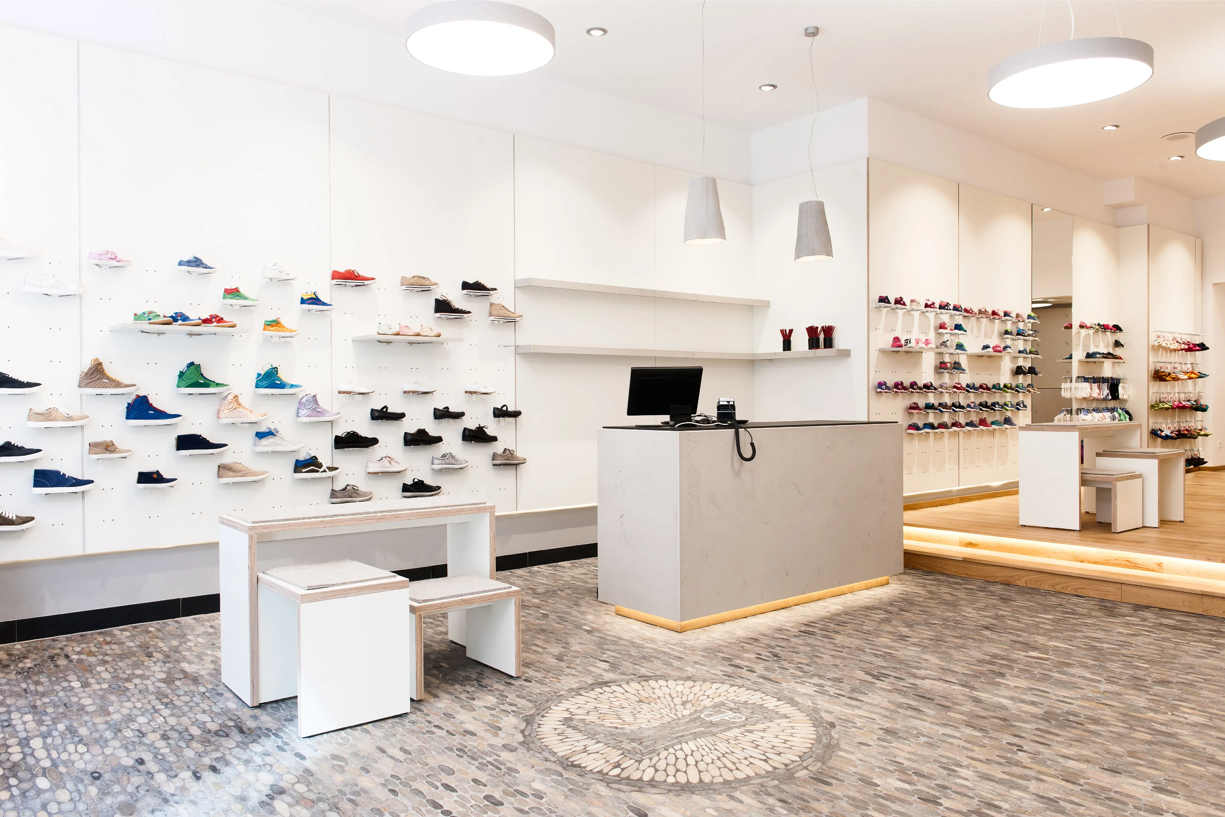 Innenansicht eines modernen Schuhgeschäfts mit Kieselmosaikboden, hellem Verkaufstresen und minimalistischem Regalsystem.