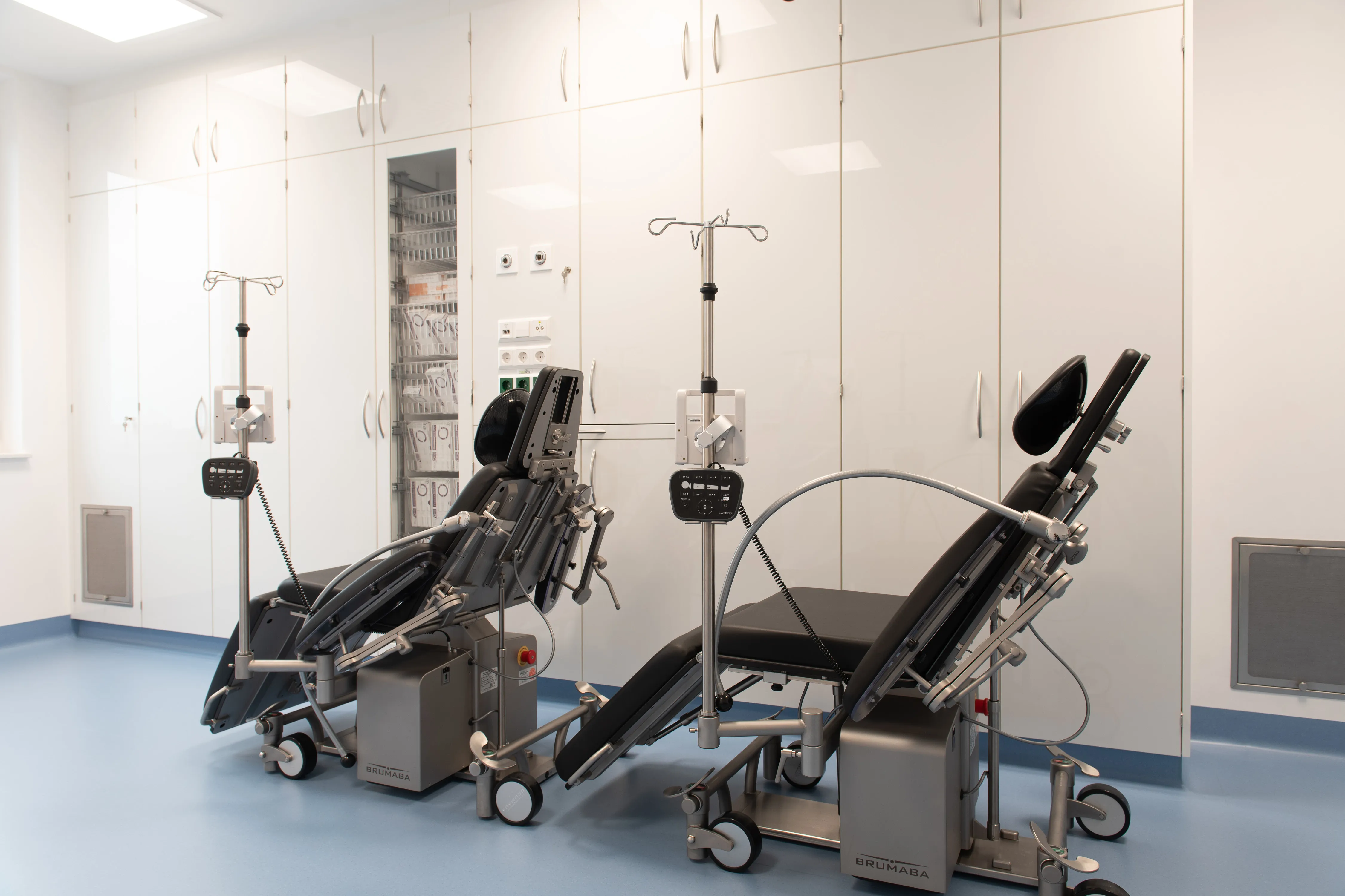 Moderner Behandlungsraum mit zwei verstellbaren Patientenstühlen vor einer raumhohen, weiß glänzenden Einbauschrankwand.