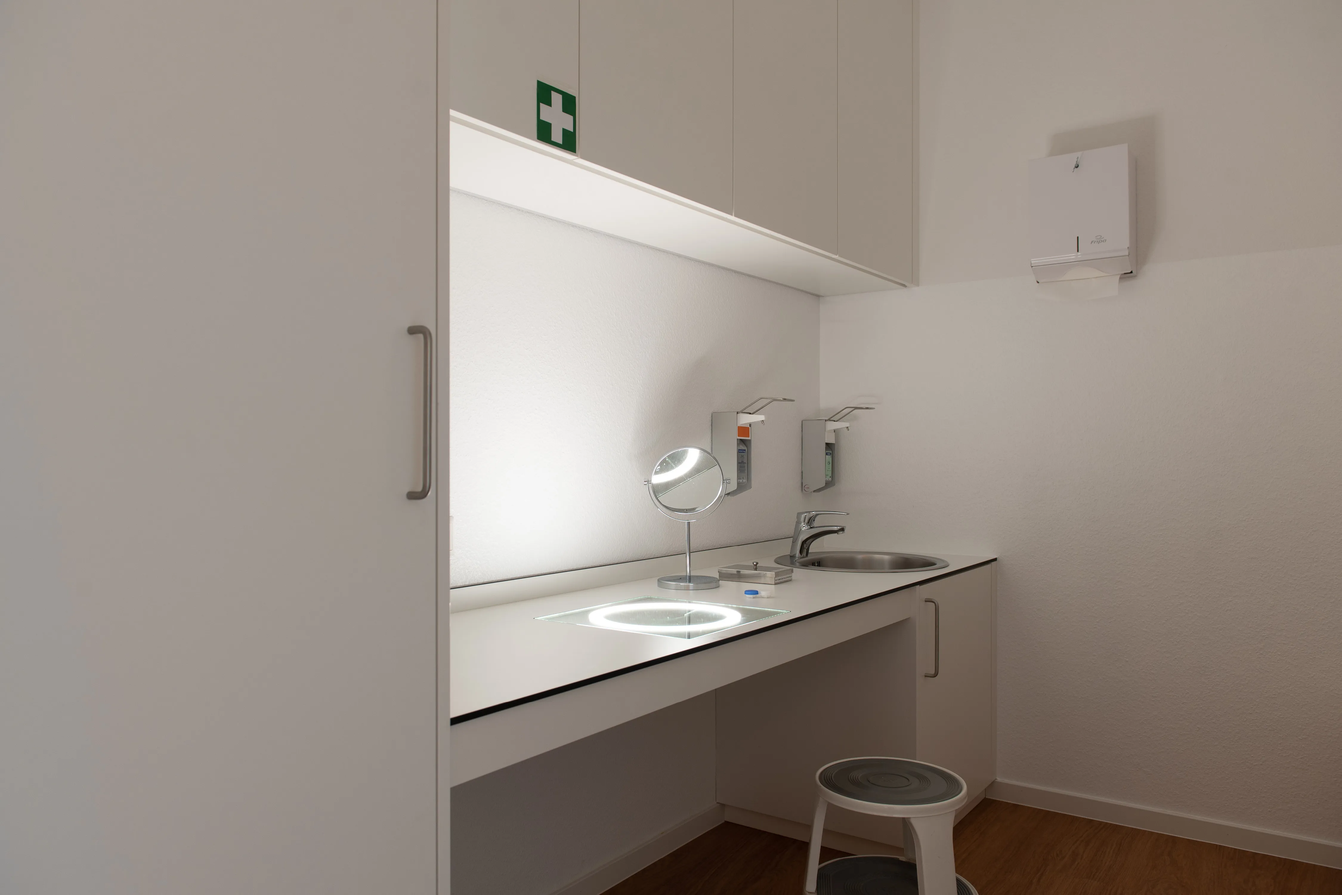 Eingebauter Kontaktlinsen-Anpassplatz mit hellem Arbeitsbereich, beleuchtetem Glaseinsatz, integriertem Waschbecken und Schrankzeile.