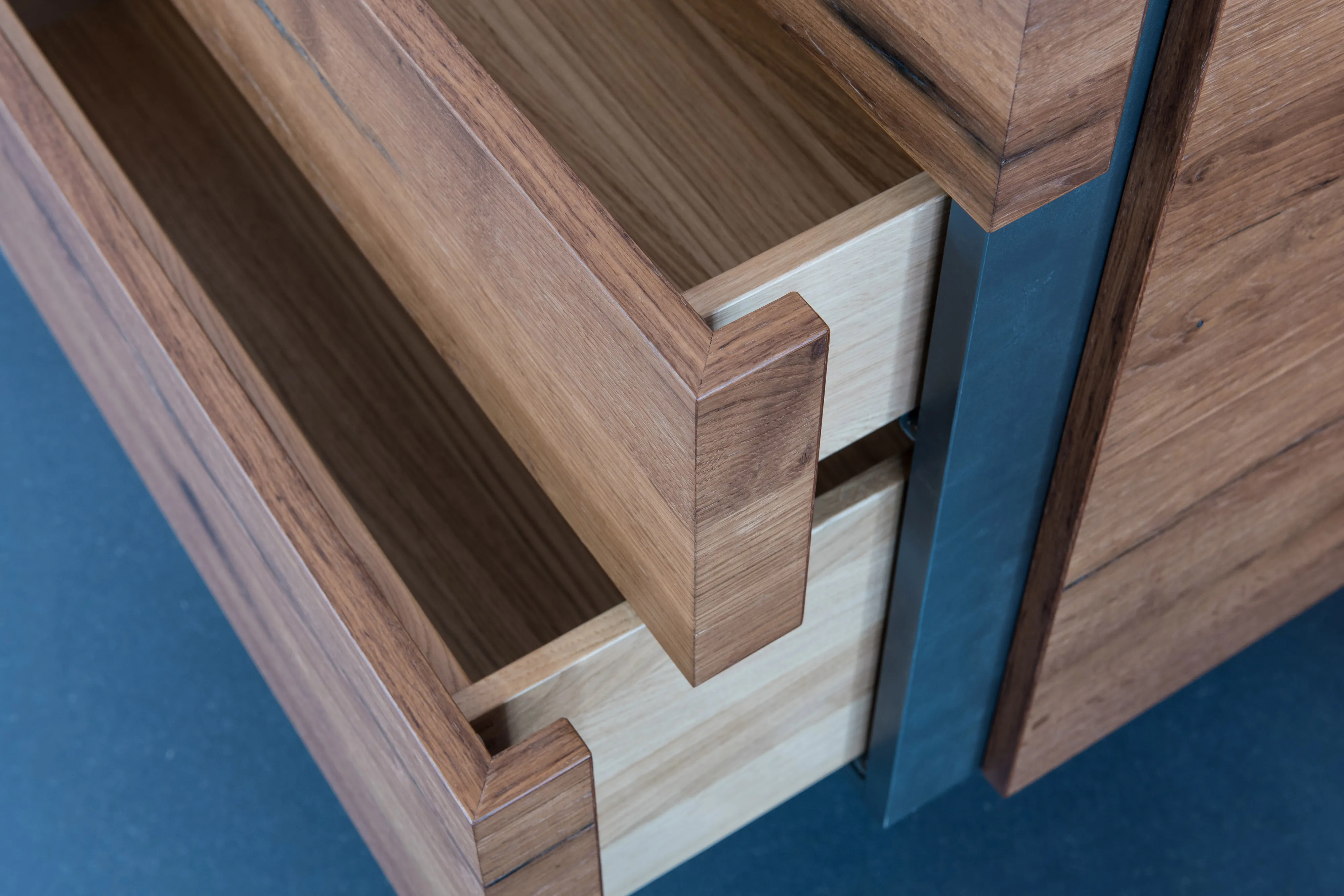 Detailansicht der geöffneten Holzschublade eines Waschtischs mit massiver Gehrungskante und integriertem Metallrahmen.