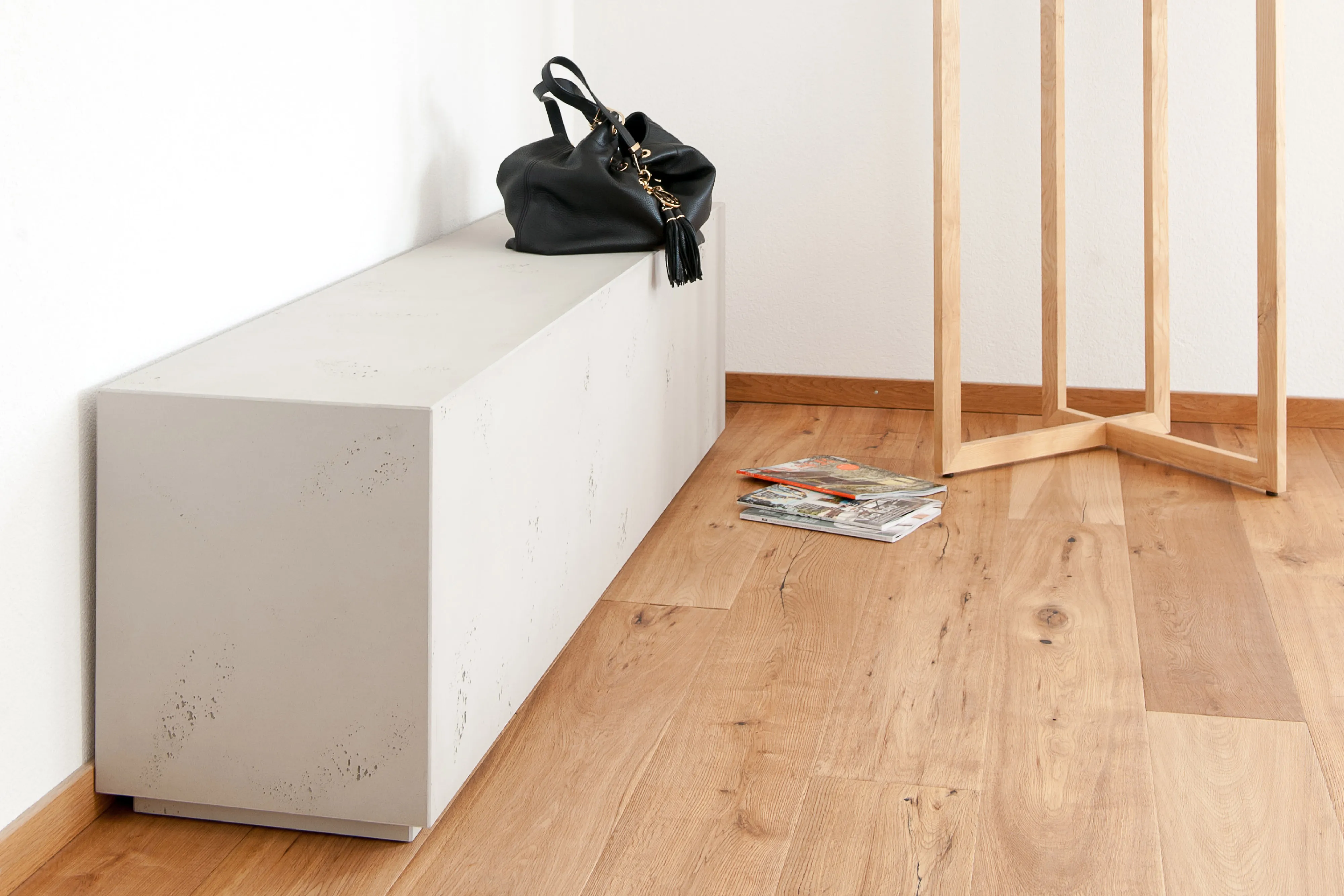 Minimalistische Sitzbank mit Betonoberflächen auf hellem Echtholzboden, kombiniert mit einem modernen Holz-Garderobenständer.