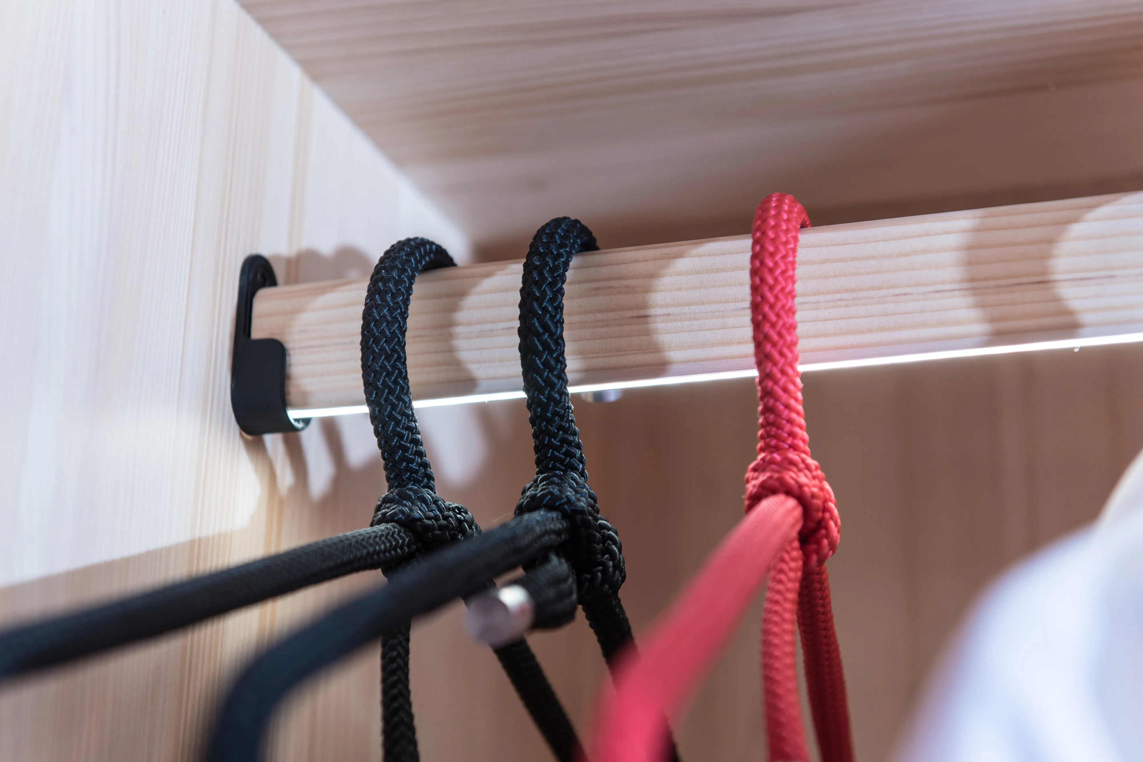 Nahaufnahme der Kleiderstange aus Holz mit integrierter LED-Beleuchtung und Kordel-Kleiderbügeln in schwarz und rot.