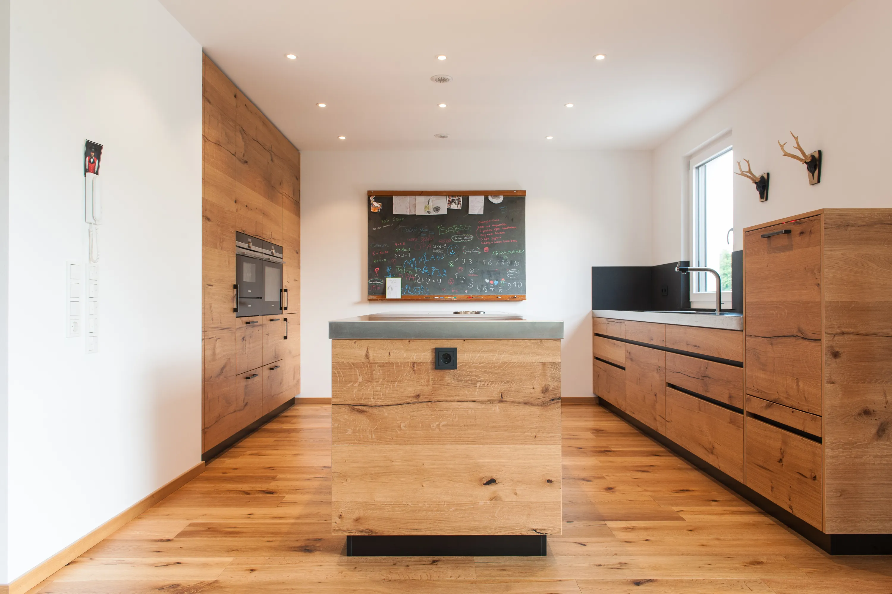 Frontalansicht einer Echtholz-Küche mit zentraler Kochinsel, Kreidetafel an der Wand und passenden Echtholzböden.
