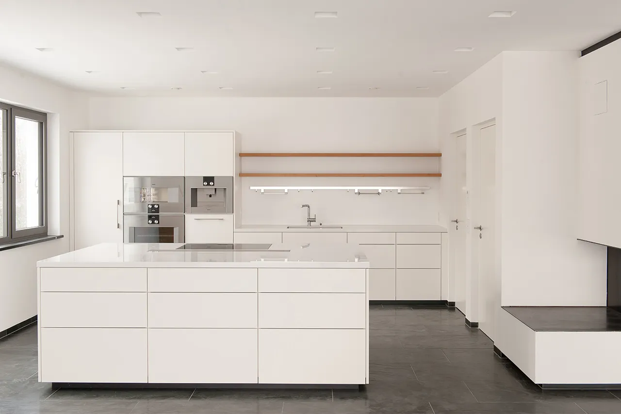 Minimalistisch gestalteter Küchenbereich in Weiß mit integrierter Sitzbank am Kamin und flächenbündigen Einbauschränken.